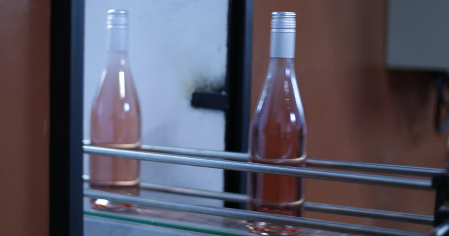 Detail of pink wine bottles going through band in line towards packaging. Beverage, production industry. Efficient quick system. Mendoza, Argentina