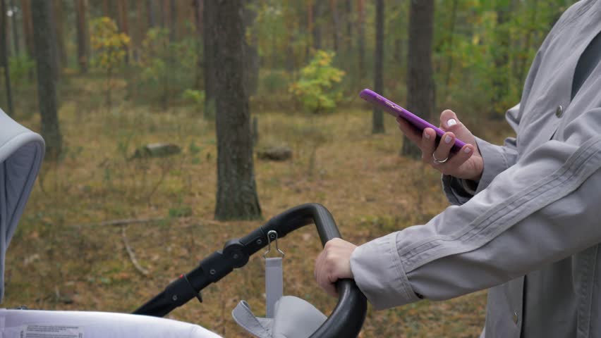 Young cute mom walking in the Park with a stroller and uses your phone