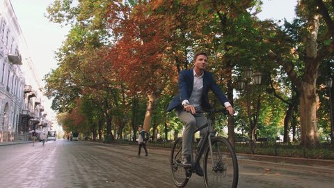 Handsome young man driving his bicycle on the street in park in city center during sunrise, slow motion Stock-video