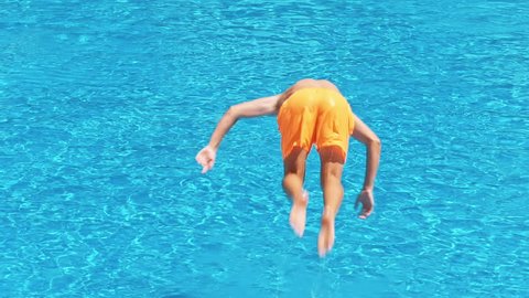 Slow motion shot of a man in blue shorts jumping in swimming pool at sunny day. Enjoying pool party with friends.