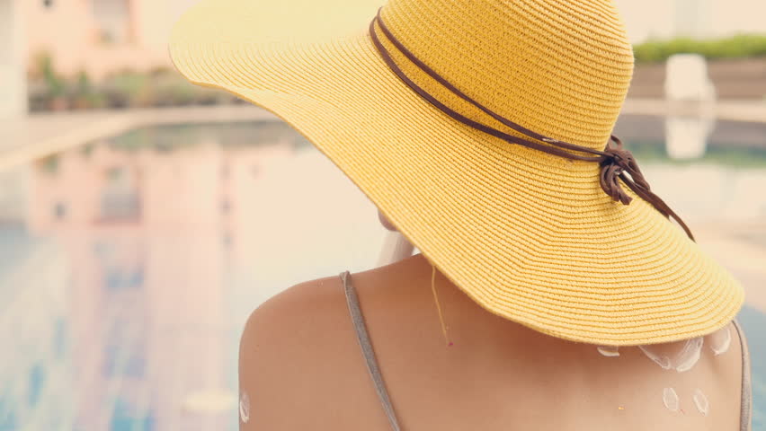 Beautiful asian woman in yellow hat sunbathing holding blank sunscreen UV protective lotion bottle packaging cosmetic template for your design at swimming pool.