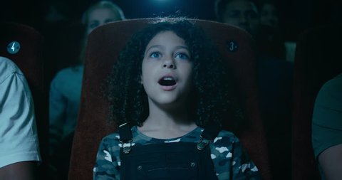 Captivated little girl in a movie theatre is awestruck by a incredible moment on screen