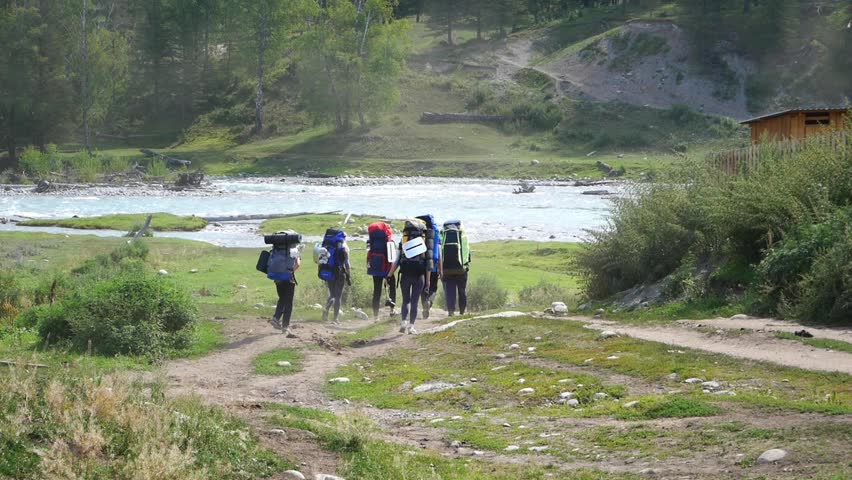 Tourists go trekking in the mountains near mountain river. 
Tourists with backpacks go on the road to the mountain across the river

