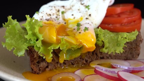 Poached egg on a piece of bread with green lettuce leaves and red tomato on a plate rotates, close up, breakfast concept