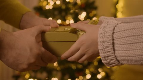 A man's hands passing a yellow gift in front of a Christmas tree