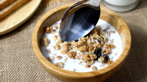 Using a spoon to mix organic cranberry and hazelnut cereal in a wooden bowl into skim milk