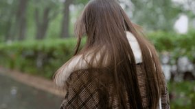 View from behind of a stylish young girl in checkered brown coat walking outside in fall.