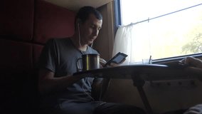 man silhouette travel is sitting on the train carriage holding a smartphone Railway and drinking coffee and tea. slow motion video. man writes messages in the smartphone in the train social media.
