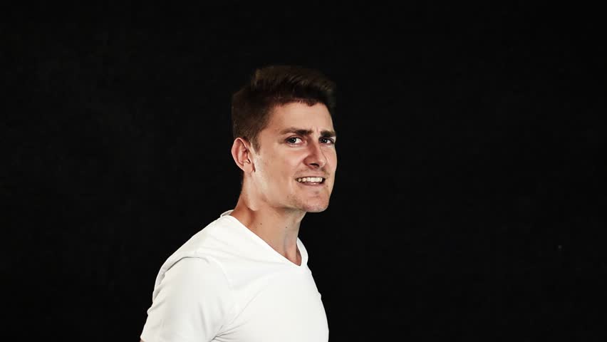 Active handsome young, slim charismatic man with big blue eyes and stylish haircut dressed in white clothes is showing dance turns with smile on face then looking at of camera on black background
