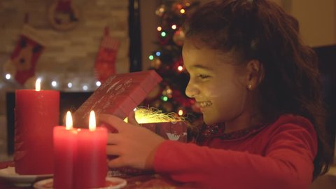 Young little girl opening gift box and looking inside with golden magic light coming from it. 