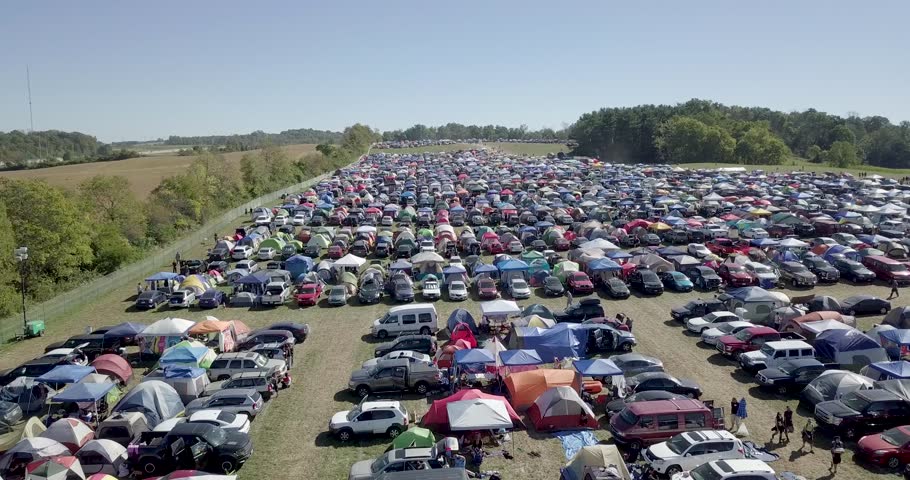 An aerial drone flight over various parts of a large outdoor music festival. Things featured, includes all the camping and parking, crowds of people moving about, different services and much more!