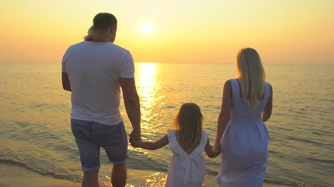 Happy family outdoors at beach sun sunset. Happy family beach summer Mother father holding hands little girl child standing on sea beach ocean. Travel Nature tourism happy holiday travelers summertime