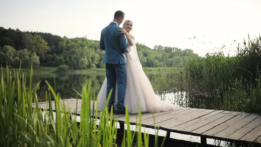 Portrait beautiful young wedding couple stand hugs near lake love bride dress groom outdoors white married woman celebration romantic beauty female man people suit husband kiss slow motion