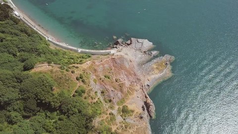 Overhead view of the beach in Torquay with its blue water and tall cliffs. Rock and woodland is visible from the sky.