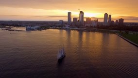 A stunning aerial drone clip pans along the serene waters of the harbor of Milwaukee Wisconsin at sunset with a stunning tall sailing ship in the foreground. Great establishing shot.