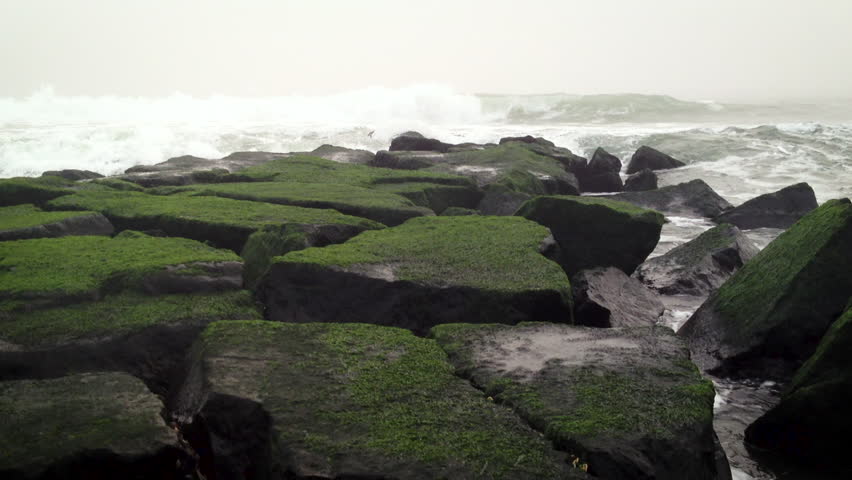 Waves crash into and flow onto of a rock jetty on the ocean shoreline.