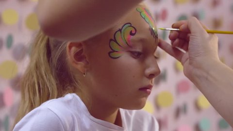 Woman making aquagrim on girl with brush, body painting on face