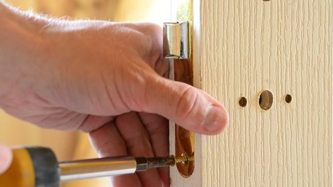 Closeup of human hands mounting a yellow golden color mortise door lock - inserting mortice doorlock into a pocket cut into white door and fixing it with screws with a screwdriver