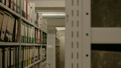 Side view between the rows of shelves of an archive. The cabinets are filled with folders.
The image can be used for the integration of archive texts in films and reports. 