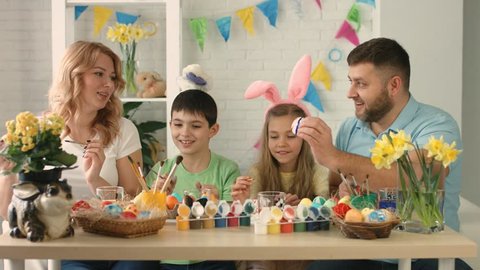 Funny family with kids wearing bunny ears painting eggs on Easter day