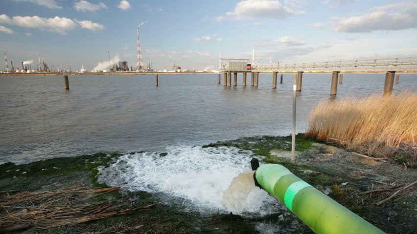 A wastewater pipe and a large oil refinery in the harbor of Antwerp, Belgium with blue sky and warm evening light.
