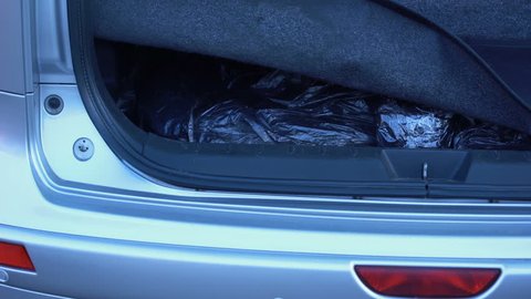 Man hiding forbidden packets in car trunk, drugs smuggling, illegal trading