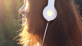 Woman listening to music in headphones with eyes closed on the outdoor. Portrait of a beautiful close-up girl.