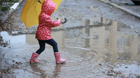 Funny child girl jumping and playing in puddles in rainy weather under an umbrella