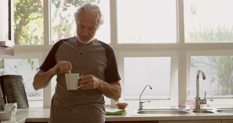 Front view of senior Caucasian man stirring coffee in kitchen at home 