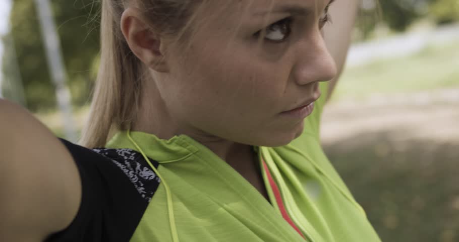 Young blond woman in fitness wear adjusting hair for running training.Summer sunny day.Industrial green city.Urban runner cardio healthy activity workout.4k slow motion 60p video