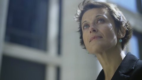 Close-up panning shot of beautiful middle aged woman with short hair and green eyes looking away in street being deep in thought