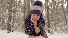 Girl in the winter forest. White snow. Joyful mood. Lying on the bench. Looking at the camera. 4K video.