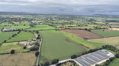 Aerial view, semi panorama panning move. Sewage works, houses among fields on Cheshire countryside. Tarvin in background