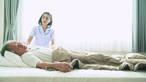 Senior man in bed trying to get up and nurse helping him. Old asian man and beautiful asian nurse woman in bedroom and open curtain. Senior home service concept. Side shot.