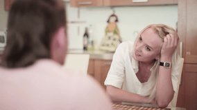 Video demonstration of brunette young man and attractive blonde woman sitting at table with bamboo mats, looking at each other and having nice warm, friendly conversation on background of kitchen.