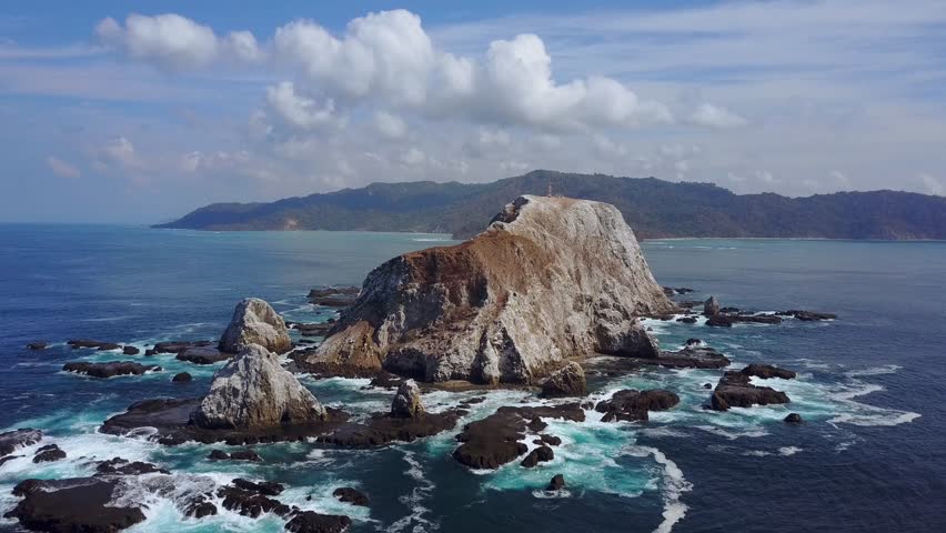 An aerial dolly shot, moving towards an Island off the pacific coast of Costa Rica, moving between the rocks, while ocean birds circle around it.