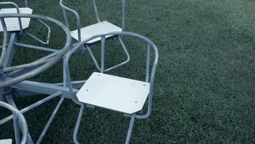 Close-up of merry-go-round seats spinning in a playground with no one in it on a rainy day, 4k