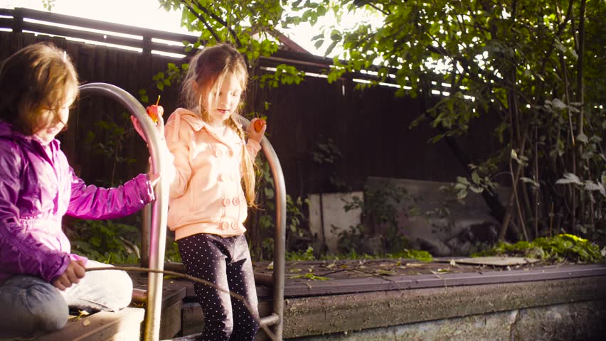 Crane shot. Two girls playing near the old pool overgrown with duckweed. They putting there orange flowers