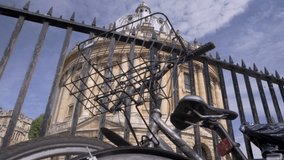 Camera rises past locked bicycle to reveal Radcliffe Camera in Oxford on a sunny summer morning
