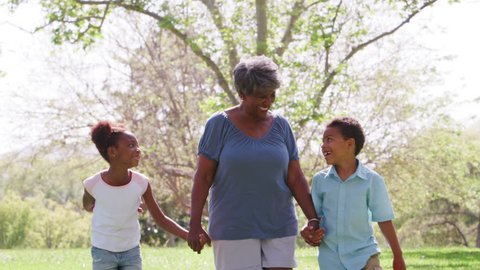 Grandmother Walking In Park And Holding Hands With Grandchildren