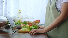 4K. woman use finger slide on tablet screen and slicing fresh lettuce, prepare ingredients for cooking follow cooking online video clip on website via tablet. cooking content on internet technology