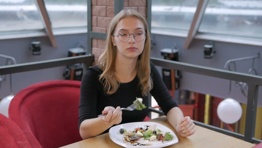 A young girl with glasses sitting in a cafe eating a Caesar salad