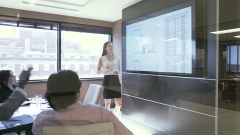 Dolly shot of businesswoman explaining data to colleagues in board room seen through glass