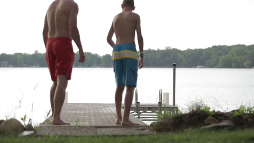 Rear view of father and son jumping from pier in lake