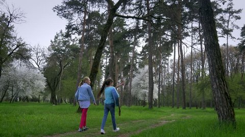 walk in the Park in springtime Two little Caucasian girlfriend with guitar in hand go on the forest path. concept of pure nature