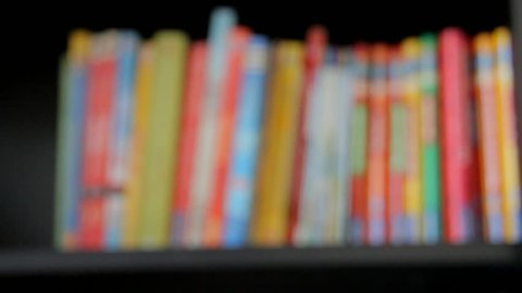 Blurred view of books on a wooden shelf. Camera moves left