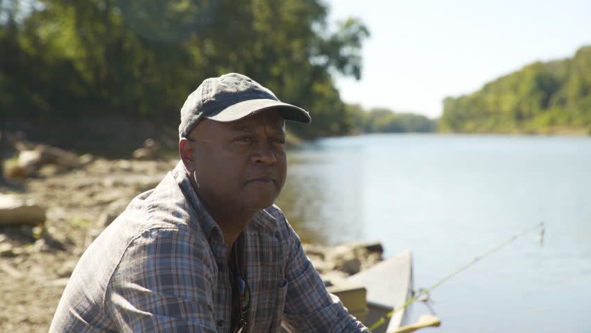 Rack focus shot of thoughtful man sitting in boat by lake in forest against clear sky