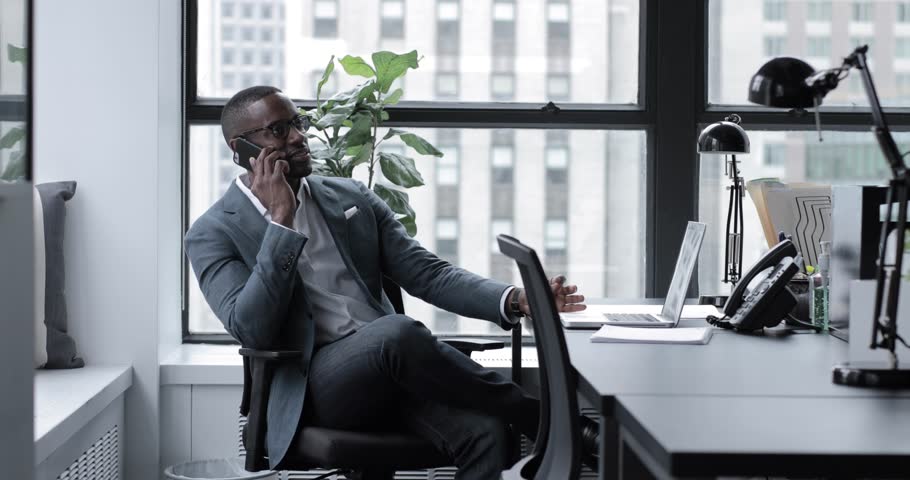 Lockdown shot of businessman answering smart phone while sitting at desk in office | Shutterstock HD Video #1016888239