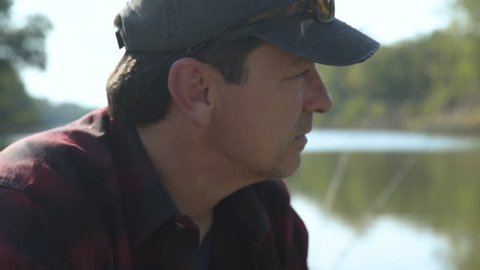 Close-up handheld shot of thoughtful man sitting on boat by lake at forest