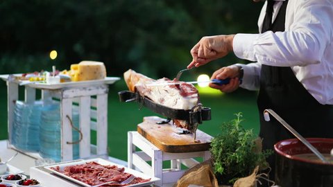 Italian waiter man cutting italian ham. Food preparation, catering. antipasto, appetizer, assortment on the table in restaurant.